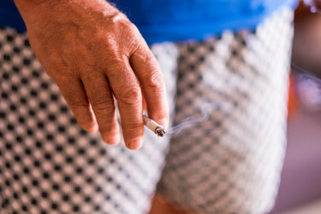 Close up of senior male hand holding a cigarette. Bad habit that is harmful to health. Wisps of smoke