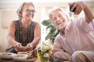 Beautiful smiles of two senior people pensioners white and gray hair looking the mobile phone for a selfie. Couple sitting outdoors on the terrace. relaxation with food and drink. Bright light.