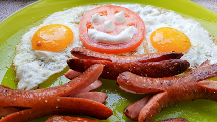 Top view of fried egg and sausages on a green plate, serving breakfast for the baby
