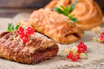 puffs with berry filling with sprigs of fresh red and white currants on burlap and dark wooden background. Close-up. Selective focus