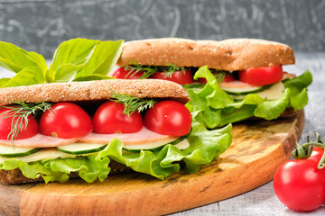 Sandwich with cheese, cucumber and Cherry Tomato on a wooden board. The sandwich is decorated with a lettuce leaf and cherry tomatoes.