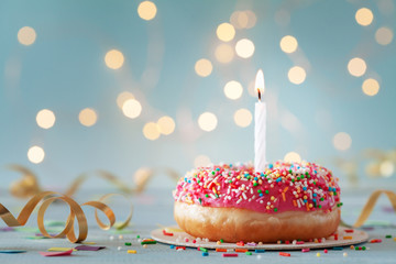 Pink donut and one burning candle against bokeh light background. Happy birthday concept.