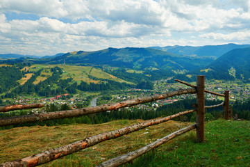 Fototapeta na wymiar Village and spruces on hills - beautiful summer landscape, cloudy sky at bright sunny day. Carpathian mountains. Ukraine. Europe. Travel background.