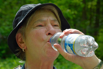 seniorin im wald trinkt aus wasserflasche