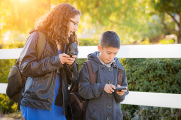 Obraz premium Hispanic Brother and Sister Wearing Backpacks Walking Texting On Cell Pones