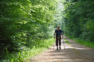 Obraz premium seniorin mit krücken geht auf einem waldweg