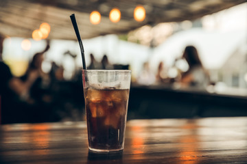 glass of cola with ice on a wooden table at an outdoor summer cafe. peoples on background
