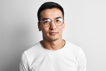 Portrait of a smart young Kazakh man in glasses and a T-shirt on a white background. Asian handsome...