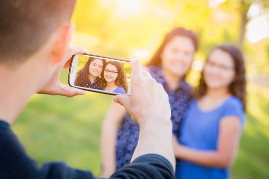 Hispanic Father Taking Picture of Mother and Daughter with Cell Phone