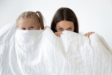 Mother and daughter hiding behind white blanket indoors