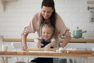 Beautiful woman helping to little daughter flattening dough
