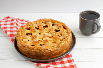 Homemade apple pie dessert with lattice and cup of tea on whiye wooden table.  Shallow focus.