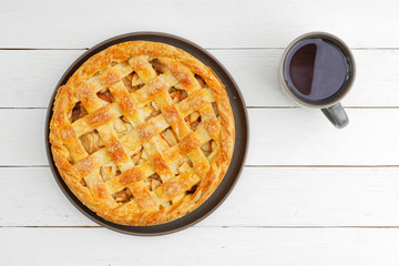 Homemade apple pie dessert with lattice and cup of tea on whiye wooden table. Top view.