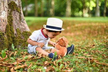 jeune garçon jouan avec un ours en peluche dans un parc