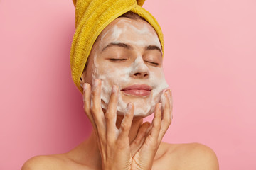 Relaxed pretty woman cares about her appearance, washes face with pleasant facial gel or soap,...
