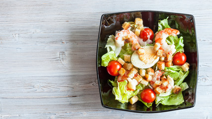 top view of Cesar salad with prawns in black bowl