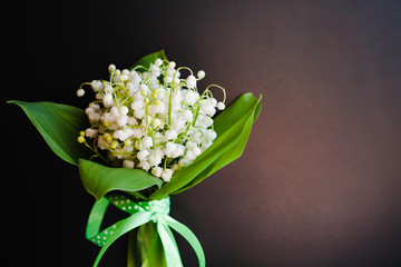Close-up bouquet of lilies of the valley tied with a green ribbon on black background. Place for text.