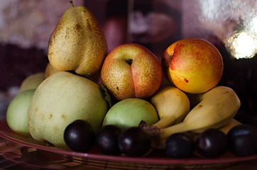 fruit on a plate with evening lighting, evening still life with apples plums pears bananas and nectarines