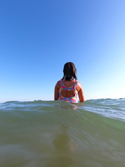 Young girl in swimsuit standing backwards and enjoying ocean water in a beach