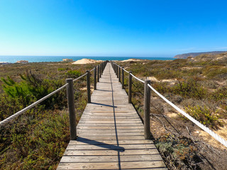 Obraz premium Wooden footpath through dunes in the Atlantic ocean coast. Guincho beach at sunset, Cascais Portugal