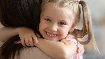 Closeup face of little cheerful daughter embraces mother