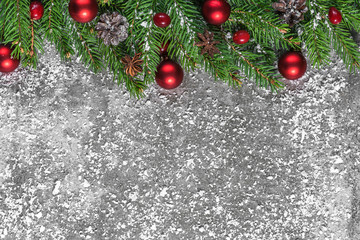 Christmas composition with fir branches, red decorations, berries and pine cones on concrete background covered with snow
