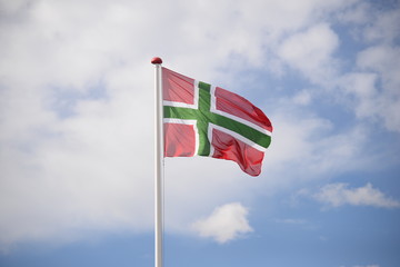 Bornholmer Flagge weht im Wind an einem weißen Fahnenmast, im Hintergrund Wolken