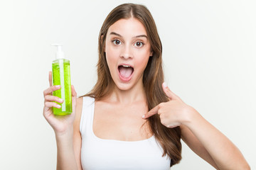 Fototapeta premium Young caucasian woman holding an aloe vera bottle surprised pointing at himself, smiling broadly.