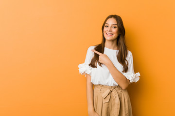 Young caucasian woman smiling and pointing aside, showing something at blank space.