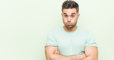 Young handsome man against a green background blows cheeks, has tired expression. Facial expression...
