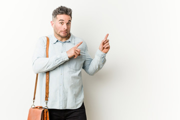 Young handsome business man shocked pointing with index fingers to a copy space.