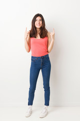 Full body young woman on white background indicates with both fore fingers up showing a blank space.