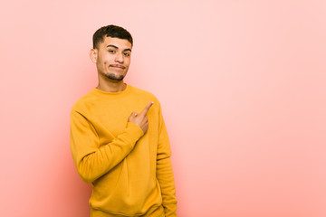 Young hispanic man smiling and pointing aside, showing something at blank space.