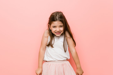 Little girl wearing a princess look laughs and closes eyes, feels relaxed and happy.