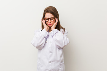 Young doctor woman against a white wall touching temples and having headache.