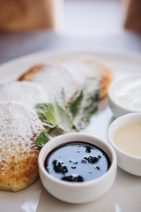 Delicious and hearty dessert, home made cottage cheese fried in a pan and served with sauces. Cheesecake, fresh jam and mint. Cottage cheese pancakes or curd fritters decorated powdered sugar in plate