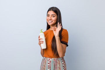 Young arab woman holding a cream bottle cheerful and confident showing ok gesture.