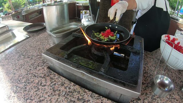 The cook prepares breakfast in a pan over an open fire A female Turkish hotel cook cooks an omelet with bacon and vegetables over an open fire