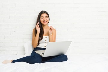 Young arab woman working with her laptop on the bed joyful laughing a lot. Happiness concept.