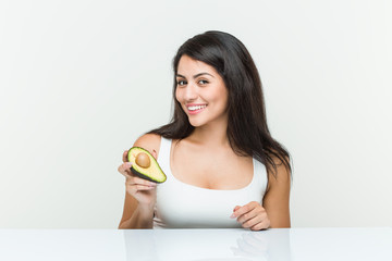Young hispanic woman holding an avocado happy, smiling and cheerful.