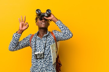 Young african tourist man standing against a yellow background holding a binoculars