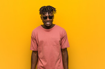 Young casual black man wearing sunglasses laughs and closes eyes, feels relaxed and happy.