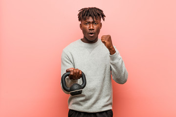 Young fitness black man holding a dumbbell showing fist to camera, aggressive facial expression.