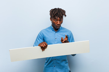 Young rasta black man holding a placard impressed holding copy space on palm.