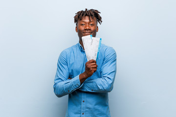 Young rasta black man holding an air tickets smiling confident with crossed arms.