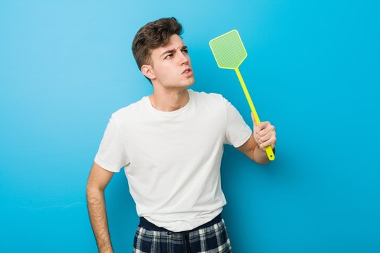Teenager caucasian man wearing pyjamas and holding a flyswatter