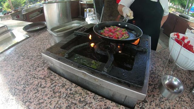 A female Turkish hotel cook cooks an omelet with bacon and vegetables over an open fire. The cook prepares breakfast in a pan over an open fire.