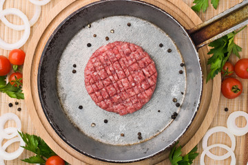 Raw Ground beef meat Burger steak cutlets in a cast iron pan on a wooden background. Burger with vegetables and spices.