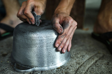 boy cleans the iron pan with his hands.  guy work with metal.