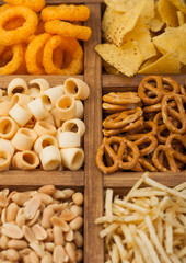 Various snacks in vintage wooden box. Onion rings,nachos, salty peanuts with potato sticks and pretzels. Suitable for beer and fizzy drinks. Macro